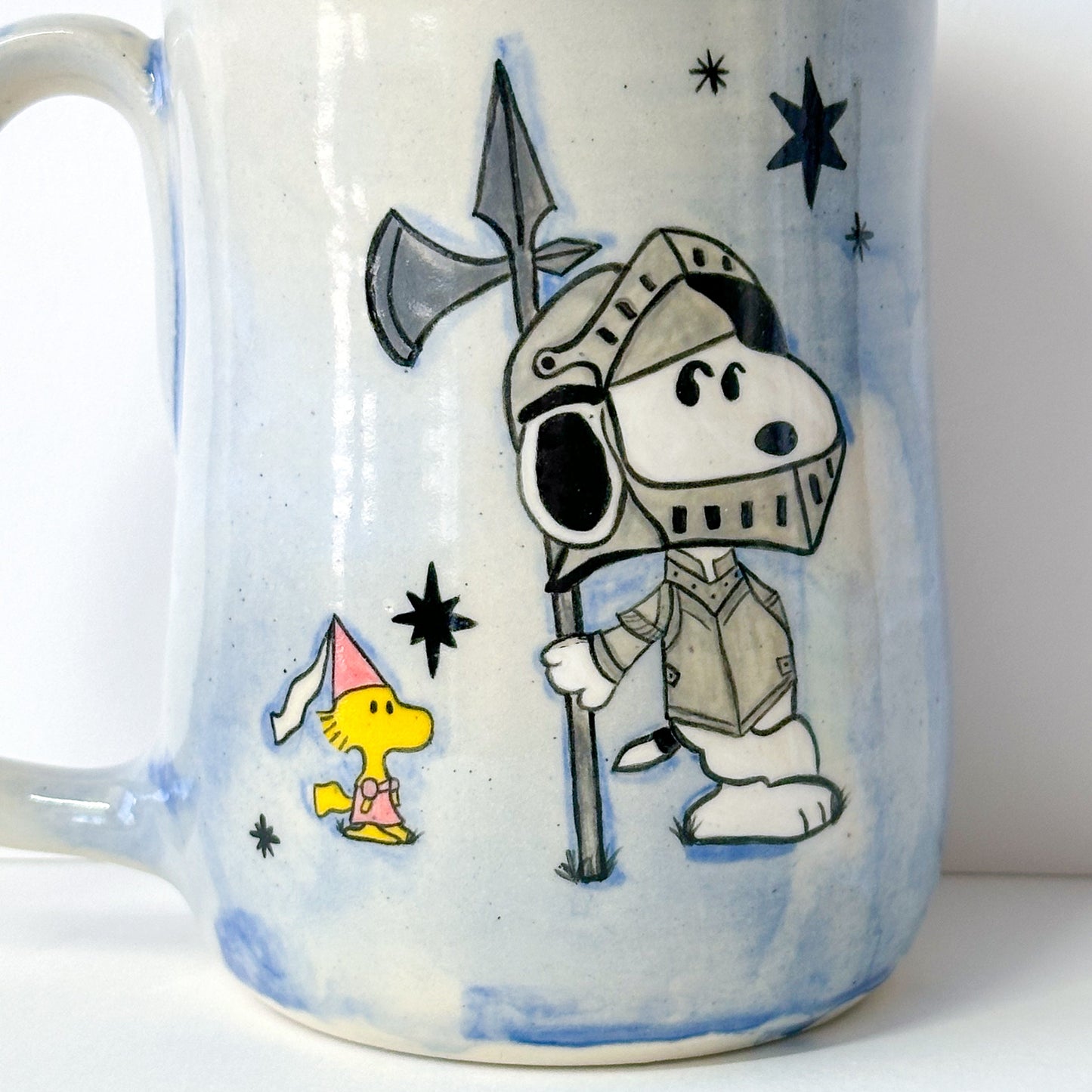 Mug with a cartoon design of Snoopy in grey armor and Woodstock in a pink dress with a princess hat, with a blue and white background.